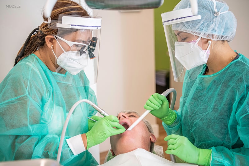 Two dental hygienists working on a dental patient wearing PPE to protect from COVID