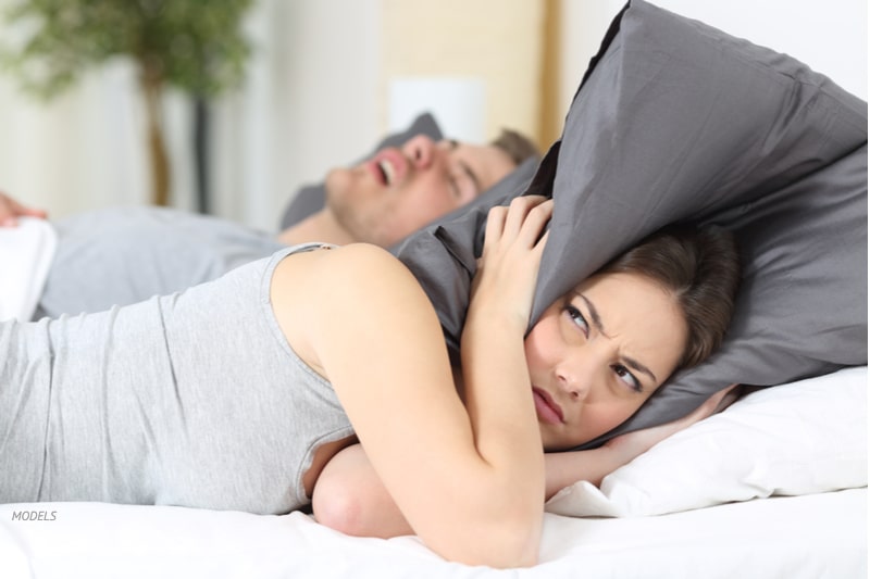 Woman covering her ears with pillows to block out partner's snoring.